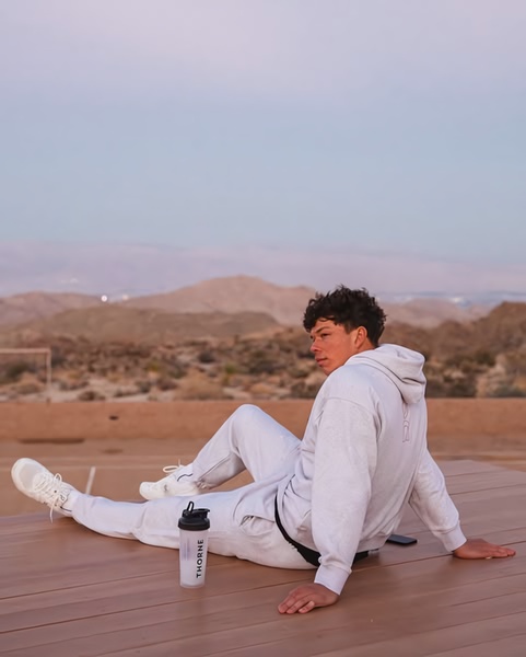 A high-quality lifestyle shot featuring a protein shaker bottle on a wooden deck overlooking desert mountains at dusk.